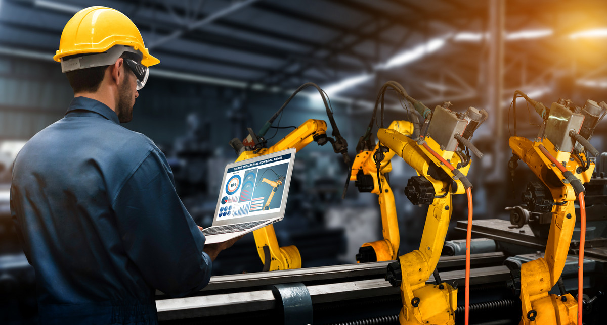 A worker with a laptop in his hands standing at a production line with many robot arms